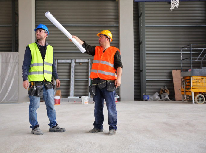 Two men wearing safety vests and helmets holding a roll of paper.