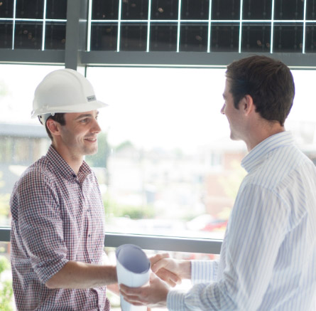 A person in a hard hat shaking hands with another person in a shirt.